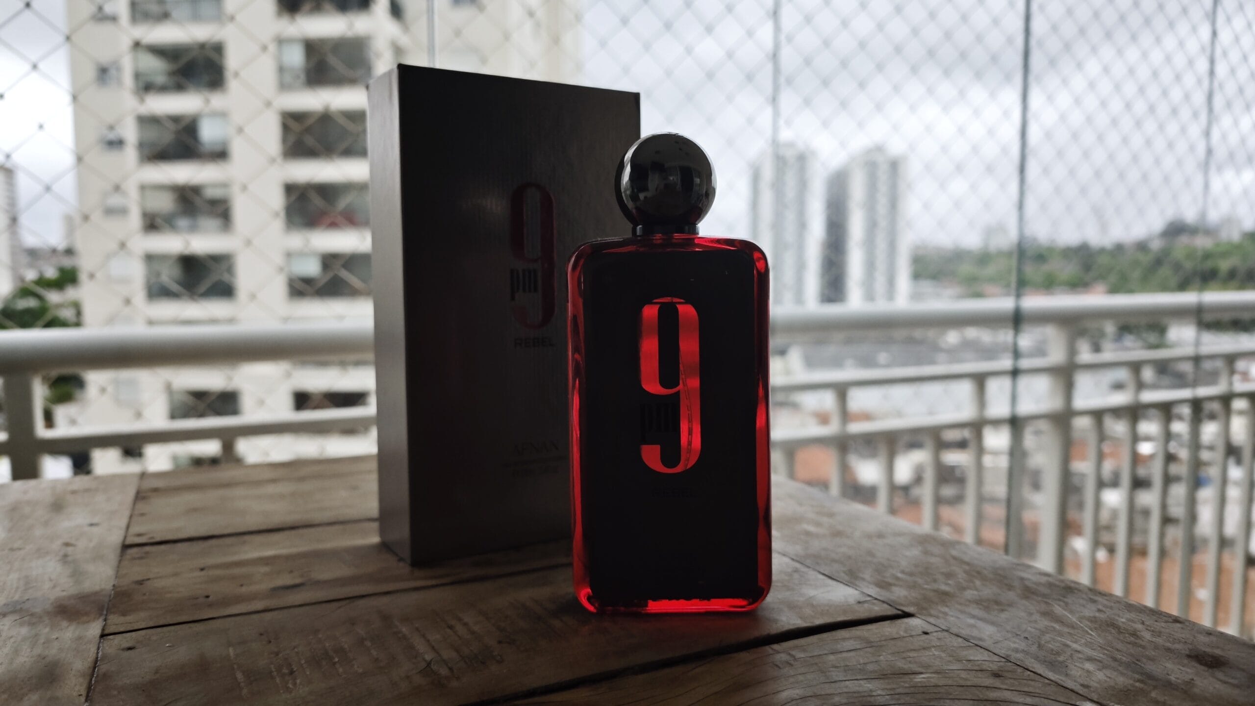 Afnan 9PM Rebel and its box on a wooden table, the city in the background