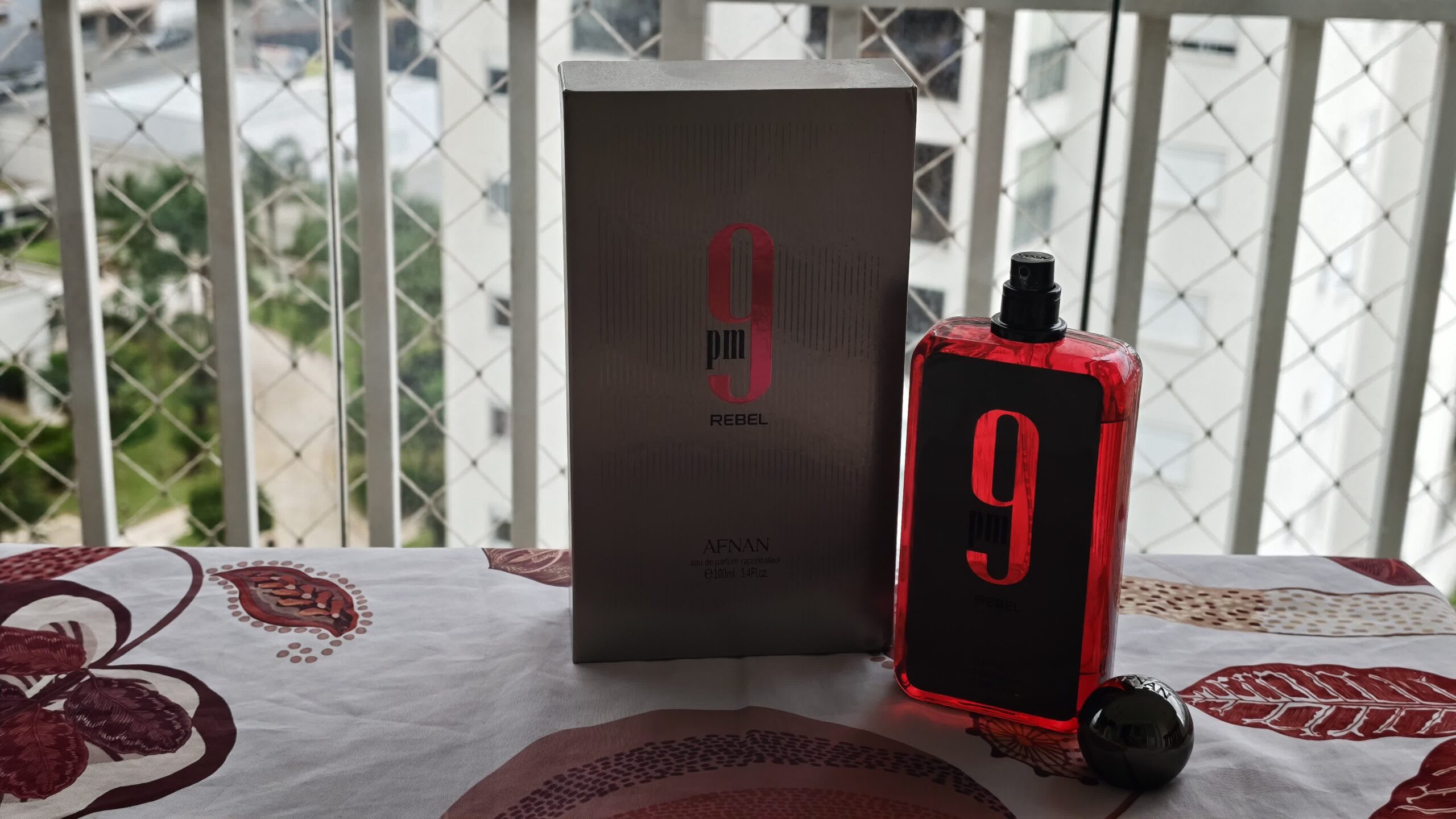The silver Afnan 9PM Rebel box in front, the open bottle beside it and the cap resting on the tablecloth